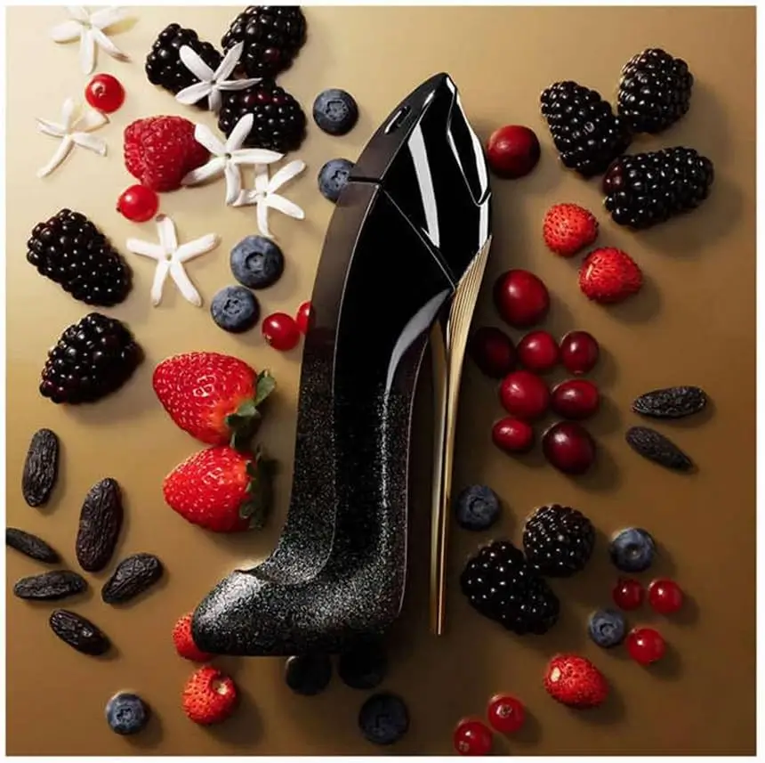 Frasco em formato de salto agulha preto brilhante do perfume Carolina Herrera Good Girl Suprême, sobre fundo elegante com elementos que evocam frutas vermelhas e notas gourmand.