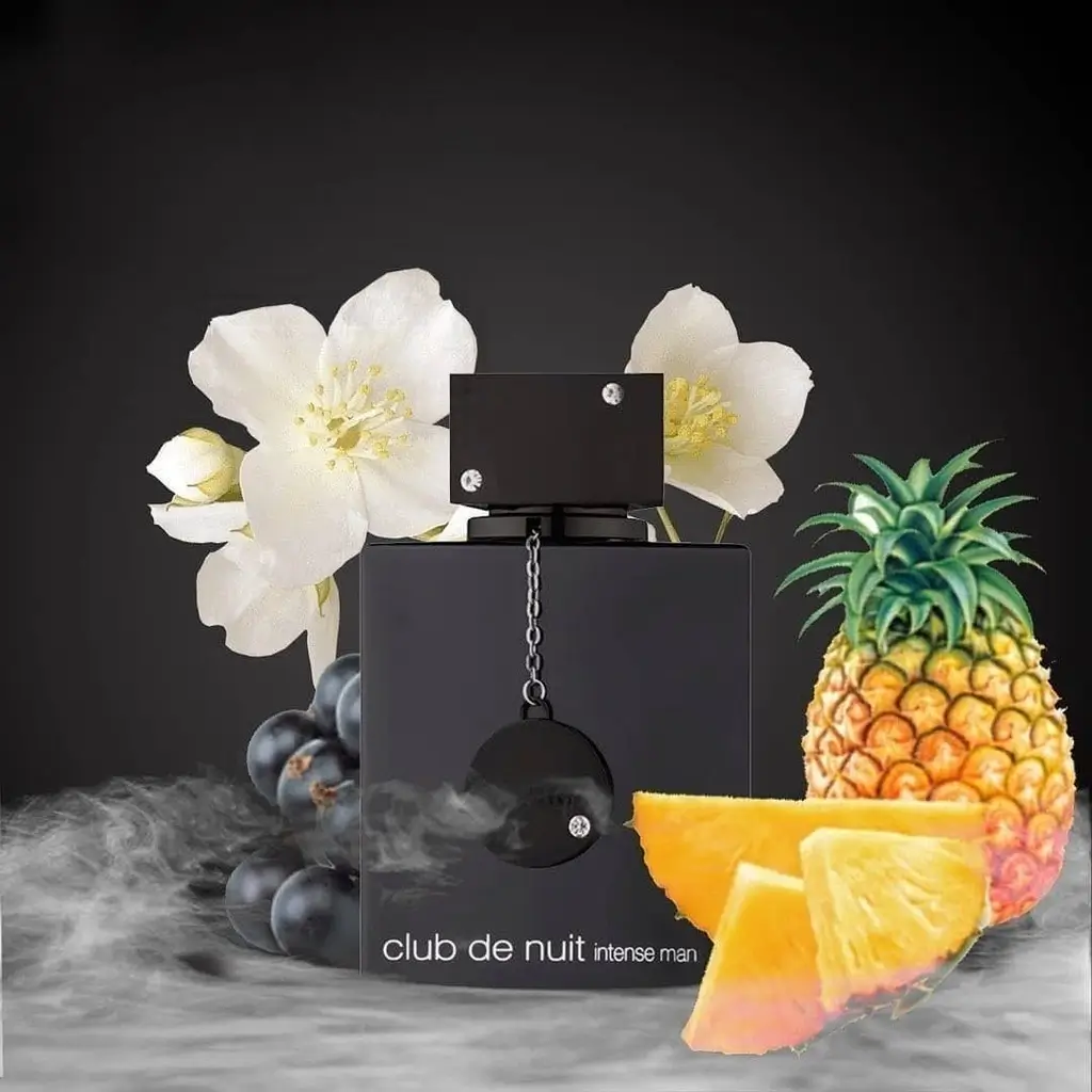 Frasco do perfume Club de Nuit Intense Man com abacaxi, flores brancas e uvas em fundo escuro com fumaça.