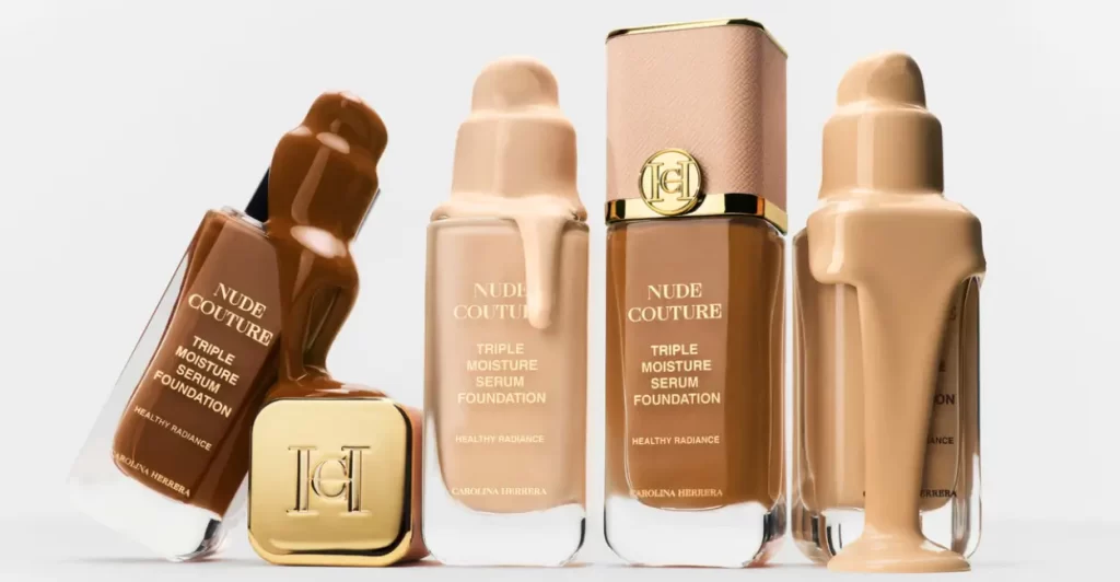 Cinco frascos da base Nude Couture Triple Moisture Serum Foundation da Carolina Herrera, em diferentes tons, com design elegante e detalhes dourados.