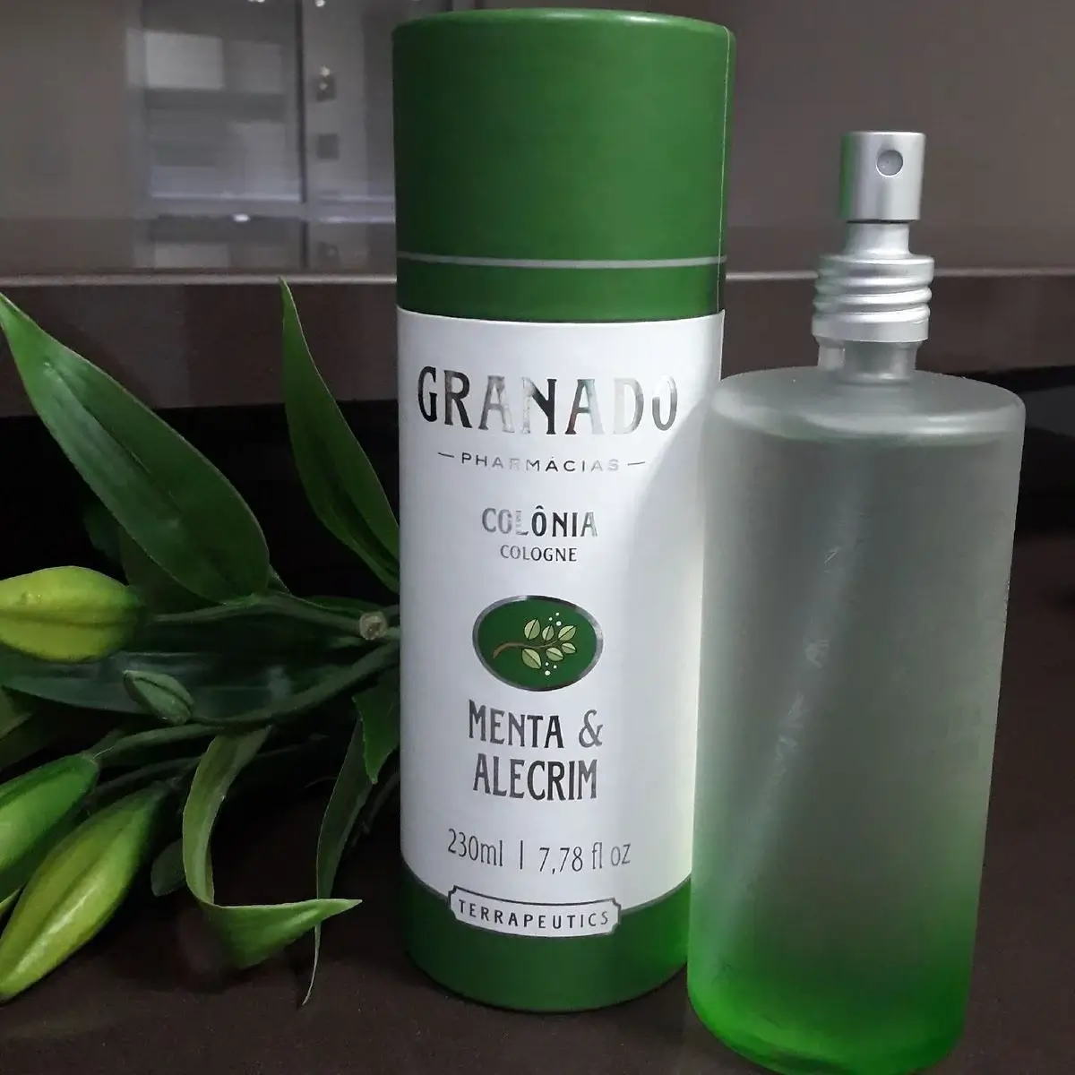 Colônia Granado Menta & Alecrim com frasco transparente ao lado de flores verdes